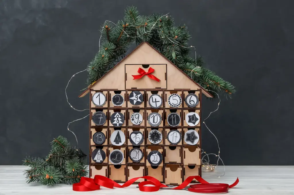 House Shaped Advent Calendar With Garland And Fir Tree On White Table
