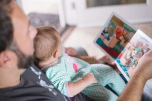 A father carrying a baby while reading a book