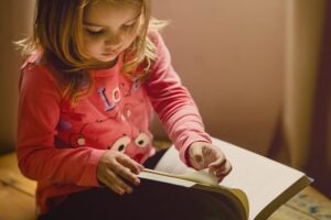 A girl wearing a pink sweatshirt reading a book