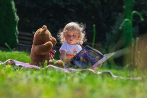 A child beside a teddy bear reading a book
