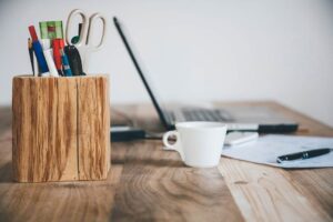 Pen holder beside a white ceramic cup and a laptop 