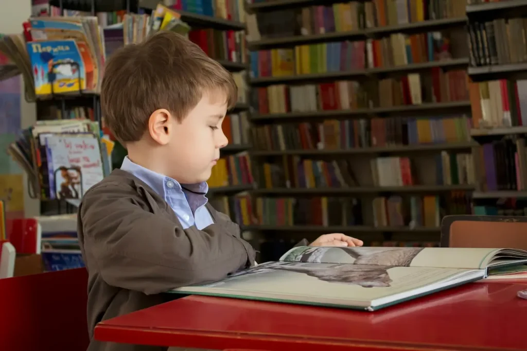 Little boy reading a book in the library 